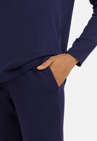 Námořnický modrý ležérní outfit skládající se z trička s dlouhým rukávem a kalhot. Tričko má volný střih a na levé straně kalhot je kapsa.