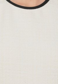 Tessuto bianco con texture e un motivo sottile, caratterizzato da un colletto rotondo nero. Il materiale appare morbido e intrecciato.