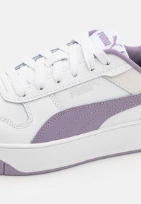 Biele kožené tenisky s svetlofialovými akcentmi, s textúrovanou podrážkou, bielymi šnúrkami a decentným logom Puma na boku.