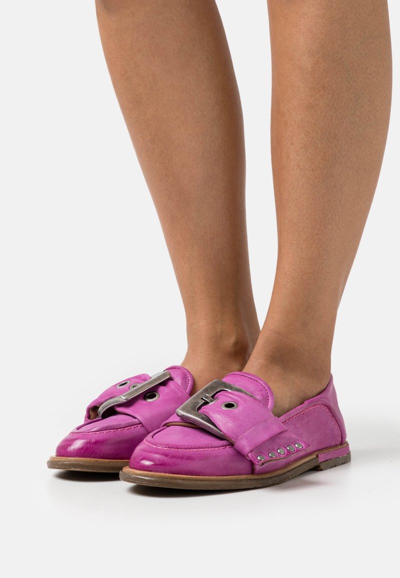 Chaussures roses en cuir à enfiler avec une grande boucle décorative, bout arrondi et accents texturés sur les côtés. Semelle plate.