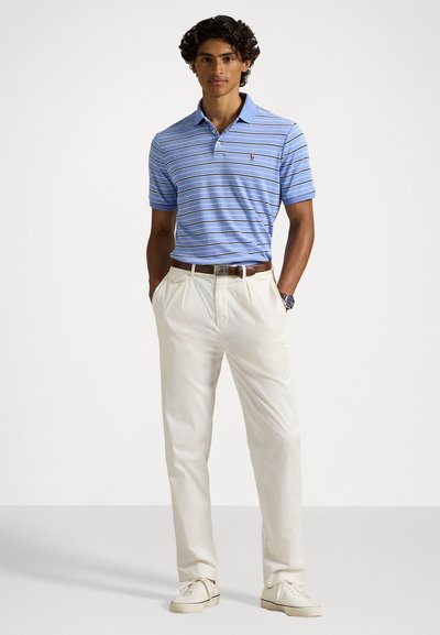 Μπλέ ριγέ πόλο μπλουζάκι με γιακά και κοντά μανίκια, συνδυασμένο με ανοιχτό μπεζ παντελόνι και άσπρα αθλητικά παπούτσια.