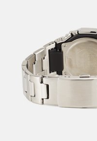 Montre en acier inoxydable argenté avec une finition brossée, dotée d'un boîtier noir, d'un bracelet à maillons et d'une fermeture à boucle.