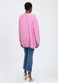 Overmaatse roze gebreide trui met een textuur, gecombineerd met lichtblauwe cropped jeans en zilveren hoge hakken.