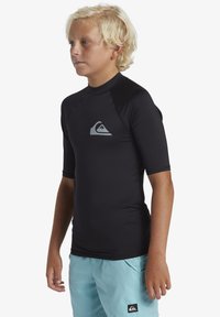 T-shirt de surf noir à manches courtes, avec un logo gris sur la poitrine, associé à un short de bain bleu clair et à un design plat.