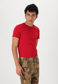 Rode aansluitende T-shirt van katoen met een ronde hals, gecombineerd met tan camouflage cargobroek met zijzakken en een knoopsluiting.