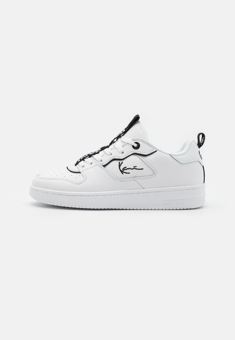 Fehér sneaker sima bőr felsőrésszel, fekete kiegészítőkkel, oldalon elhelyezett jellegzetes logóval, lekerekített orral és kontrasztos fűzőkkel.