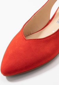 Red suede flat shoe with a pointed toe and V-shaped cutout at the front. Smooth inner lining and minimalistic design.