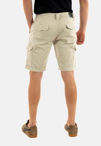 Pantaloni cargo beige con tasche laterali, orli arrotolati e taglio classico, realizzati in robusto tessuto di cotone. Indossati con scarpe marroni.