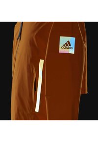 Oranger Sportjacke mit reflektierenden Akzenten, zippered Tasche und Adidas-Logo am Ärmel. Glatte Textur, taillierte Passform.