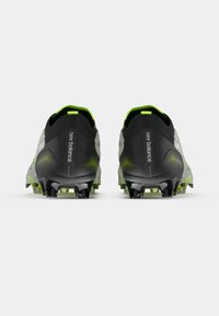 Mustat ja neonvihreät New Balance -jalkapallosukat nähtynä takaa, jossa on piikkipohjat valkoista taustaa vasten.