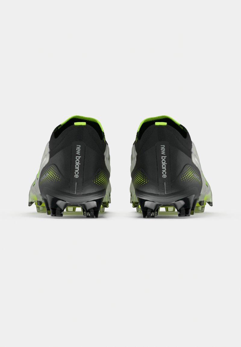 Un paio di scarpini da calcio New Balance neri e verde neon visti da dietro con suole chiodate su uno sfondo bianco.