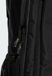 Svart ryggsäck med ett texturerat tyg, utrustad med en mjuk dragkedja och dragsnören, samt en detalj med nätficka på sidan.