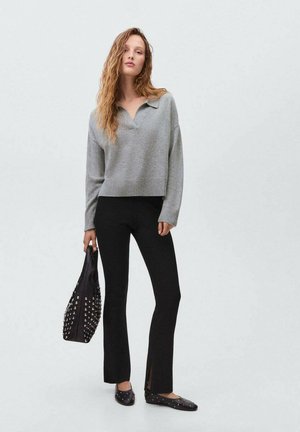 Pullover grigio a maglia con scollatura a V, abbinato a pantaloni neri a coste svasati con spacchi laterali. Gli accessori includono una borsa nera con borchie.