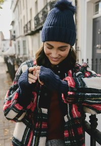 Navy beanie z mieszanki wełny z pomponem, czerwona i czarna w kratę polarowa kurtka, granatowe rękawiczki bez palców i tekstura prążkowana. Zapięcie na guziki.