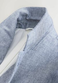 Gros plan sur le col et le revers d'une veste en tissu tissé bleu clair, avec une doublure intérieure blanche.