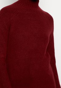 Punainen korkea kauluksellinen neulepaita, joka on valmistettu pehme ästä ja paksusta neulemateriaaliasta. Sisältää istuvan siluetin ja ribbausta kauluksessa sekä helmassa.