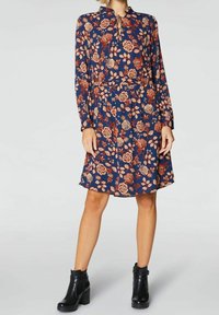 Granatowa sukienka w kwiaty z długimi rękawami i wiązanym dekoltem. Posiada czerwone i kremowe kwiaty oraz liście. Zestawiona z czarnymi botkami za kostkę.