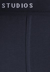 Navy ribbed leggings with a wide elastic waistband featuring the text "STUDIOS" in white. Smooth texture and fitted shape.