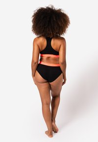 Soutien-gorge de sport noir et culottes taille haute assorties avec le texte rouge "HAPPY SHORTS" sur la ceinture, texture lisse, design minimaliste.