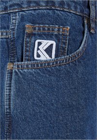 Denim jeans med en klassisk blå farge, synlig søm og en liten hvit brodert logo på baklommen.
