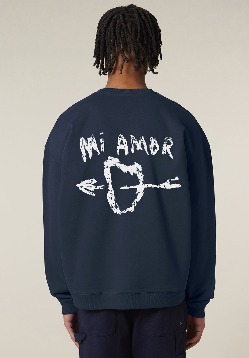 Felpa navy con grafica bianca che riporta il testo "Mi Amor", con un design a forma di cuore e freccia sul retro. Realizzata in un tessuto morbido, con una vestibilità comoda.