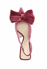 Chaussure à talon haut en velours rose avec un bout pointu et un large nœud décoratif. Dispose d'une fine sangle à la cheville et d'une semelle intérieure rembourrée beige.