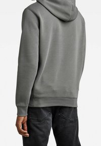 Sudadera gris con un acabado texturizado, que incluye capucha, puños y dobladillo acanalados. Combinada con jeans oscuros, mostrando un ajuste casual y relajado.