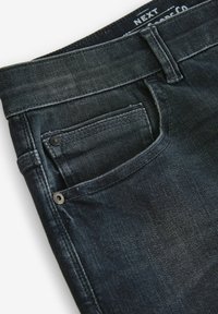 Sötétkék farmernadrág klasszikus szabással, elülső zsebből, fém részletekkel és enyhén kopott textúrával.