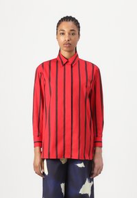 Camicia rossa a maniche lunghe con strisce verticali nere, dotata di colletto a punta e polsini con bottoni. Tessuto liscio con una vestibilità strutturata.