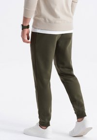 Olijf groene sweatpants hebben een taps toelopend ontwerp met zijzakken, ribgebreide boorden en worden gedragen met witte sneakers. Gladde stofstructuur.