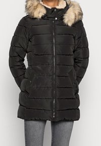 Černá péřová bunda na zip s horizontálním prošíváním, kapucí s kožíškem a bočními kapsami se cvoky. Měkká a hladká tkanina.