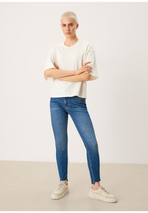 Camiseta blanca de mangas cortas combinada con jeans skinny azules y zapatillas beige con una suela de plataforma texturizada. Diseño simple y limpio.