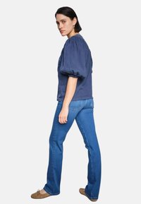 Navy puff-sleeve top paired with blue flared jeans. Cotton material, smooth texture, and a fitted silhouette. Brown flat shoes.