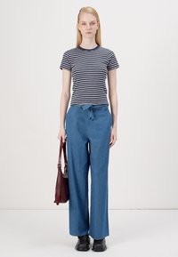 Striped navy and white t-shirt, relaxed blue wide-leg trousers with a tie waistband, and black ankle boots. Model holding a burgundy bag.