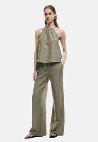 Conjunto de dos piezas en lino de color verde oliva que incluye una blusa de cuello halter y pantalones de pierna ancha con cintura ajustable. Textura y diseño sencillos.