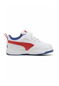 Zapatilla deportiva de cuero blanco con detalles en rojo y azul, tira de velcro, forro azul, puntera perforada y suela texturizada. Diseño minimalista.