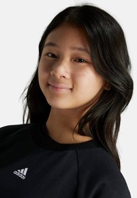 Sudadera negra con cuello redondo y mangas largas, que presenta un logo blanco de Adidas en el pecho. Tejido suave con un corte relajado.