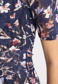 Marineblaues Spitzenkleid mit Blumenmuster, kurzen Ärmeln, strukturierter Stoff mit rosa, weißen und violetten Blumenmustern sowie Raffungen an der Taille.