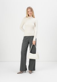 Hvit, stripete langermet topp med bølget kant, kombinert med grå vide bukser. Modellen holder en hvit håndveske med snøring.