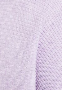 Gros plan sur un tissu en maille côtelée douce de couleur lavande claire avec des lignes texturées horizontales et verticales montrant des coutures détaillées.