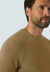 Beige gebreide trui met een geribbelde textuur, ronde halslijn en raglanmouwen, die een soepele afwerking en comfortabele pasvorm benadrukt.