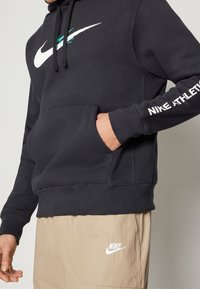 Sweat à capuche noir Nike avec un grand logo blanc et des accents verts d'eau. Comprend une poche kangourou à l'avant et des poignets côtelés aux manches et à l'ourlet.
