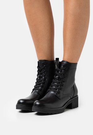 Bottes chelsea en cuir noir à lacets sur le devant et fermetures éclair latérales, portées sur jambes nues, avec talons épais et semelles épaisses.