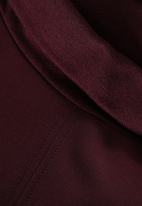 Burgundy pulóver puha, textúrált anyagból, magas nyakkal és látható varrásokkal, sima, meleg megjelenést kölcsönöz.