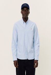 Light blue button-up shirt with collar, long sleeves; red embroidered "II" on the chest. Navy cap with white script text.