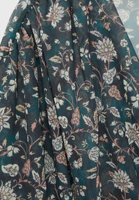 Tissu vert foncé avec des motifs floraux beige, rose et blanc, drapé en plis doux, montrant la texture et des dessins complexes de fleurs et de feuilles.
