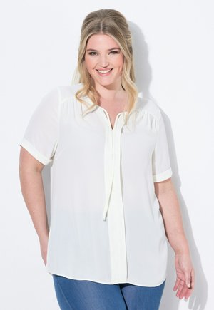 White short-sleeve blouse with a V-neck and tie detail, featuring a smooth, lightweight fabric and subtle gathered accents at the shoulders.