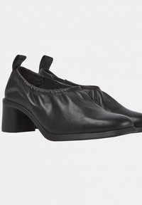 Bottes cheville en cuir noir avec un bout pointu, un design froncé au niveau de la cheville et un talon épais. Texture lisse et détails de couture subtils.