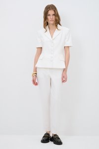 Witte op maat gemaakte blazer met korte mouwen, grote knopen en zakken, gecombineerd met bijpassende witte broek en zwarte instappers.