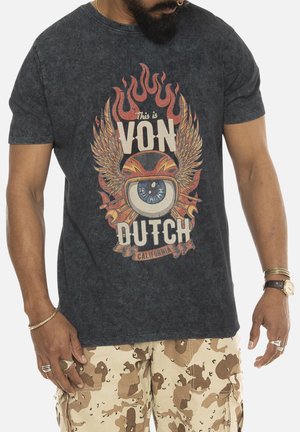 T-shirt graphique noir en coton, avec un logo central comportant des ailes, des flammes et du texte. Le tissu a une texture légèrement usée.